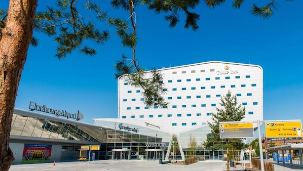 An airport terminal building with a modern glass facade and a sign indicating the terminal and parking areas.