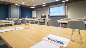 A conference room with tables, chairs, a projector screen, and a presentation board.