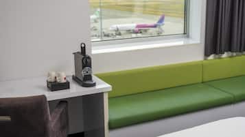 Habitación de hotel con vista a un aeropuerto, una mesita con cafetera y un banco verde.