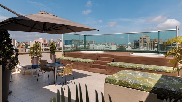 Una terraza en la azotea con barandilla de vidrio, mobiliario exterior y plantas en macetas.