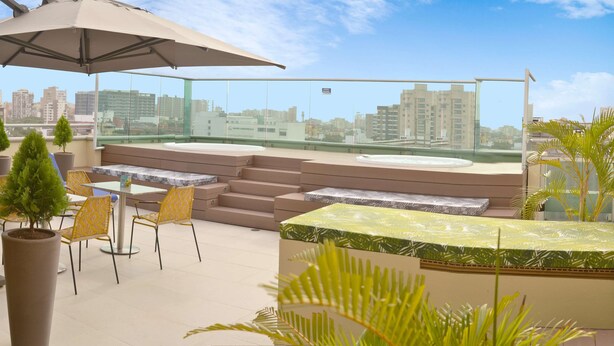 Una terraza en la azotea con asientos al aire libre, un paraguas grande y vistas de la ciudad.