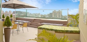 A rooftop terrace with outdoor seating, a large umbrella, and city views. - Hampton by Hilton Barranquilla (Barranquilla)