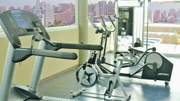 A gym with cardio machines and a view of a cityscape through large windows.