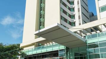 A modern hotel with a prominent 'Hampton' sign, a glass facade, and a rooftop terrace.