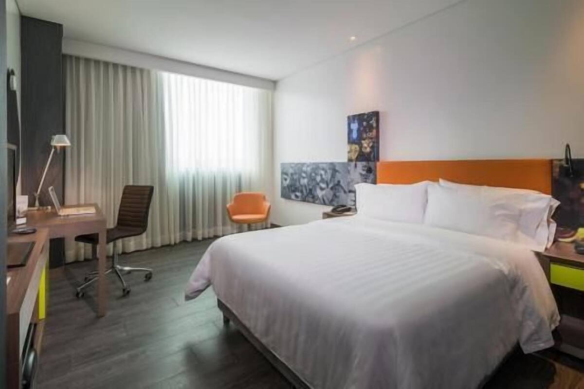 A hotel room with a bed, a desk, a chair, and a window with curtains.