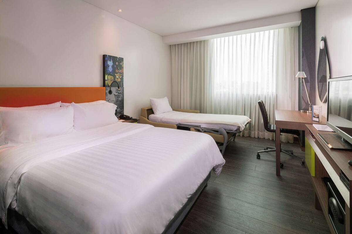 A hotel room with two beds, a desk, a chair, and a large window with curtains.