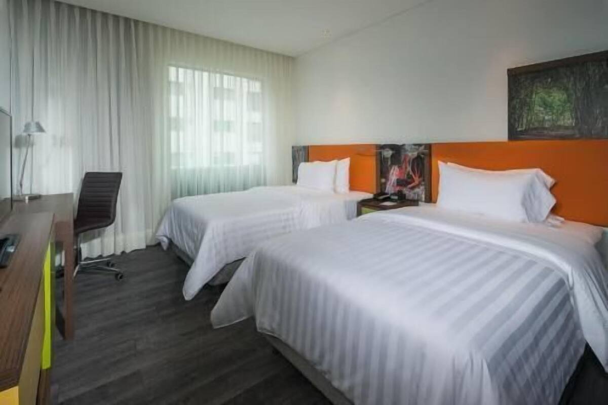 A hotel room with two beds, a desk, a chair, and a painting on the wall.