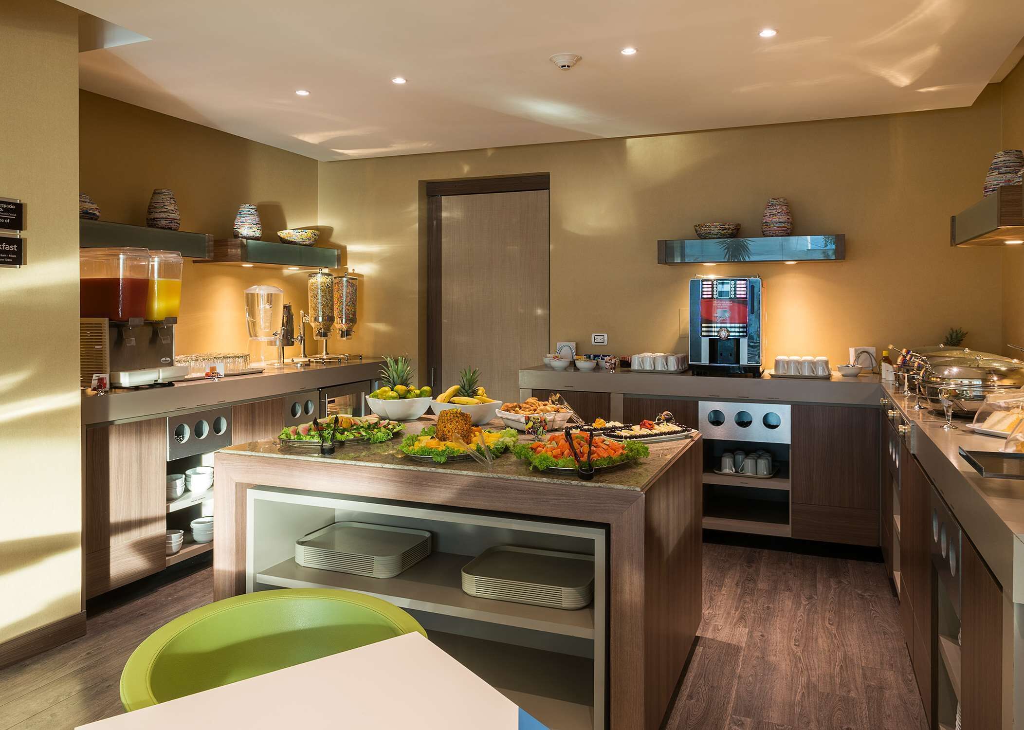 Una cocina moderna con una barra libre, que incluye una cafetera, cuencos de fruta y diversas opciones de comida.