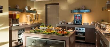 A modern kitchen with a buffet setup, including a coffee machine, fruit bowls, and various food items.
