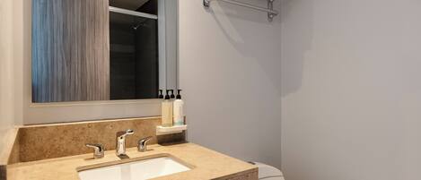 Un baño con un lavabo color crema, dos grifos, un espejo, un perchero para toallas y un inodoro.