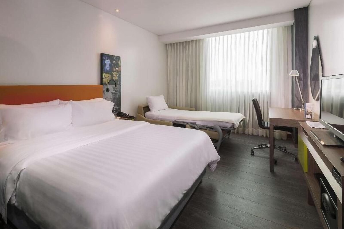 Una habitación de hotel con dos camas, un escritorio, una silla, un televisor y una ventana con cortinas.