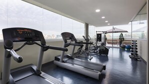 Un gimnasio con cintas de correr, bicicletas estáticas y pesas.