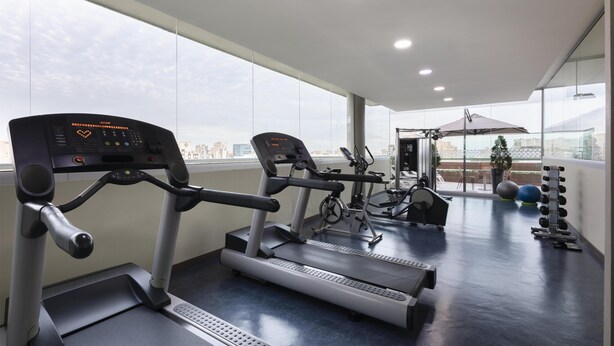 Un gimnasio con cintas de correr, bicicletas estáticas y pesas.