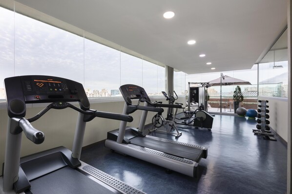 Un gimnasio con cintas de correr, bicicletas estáticas y pesas.