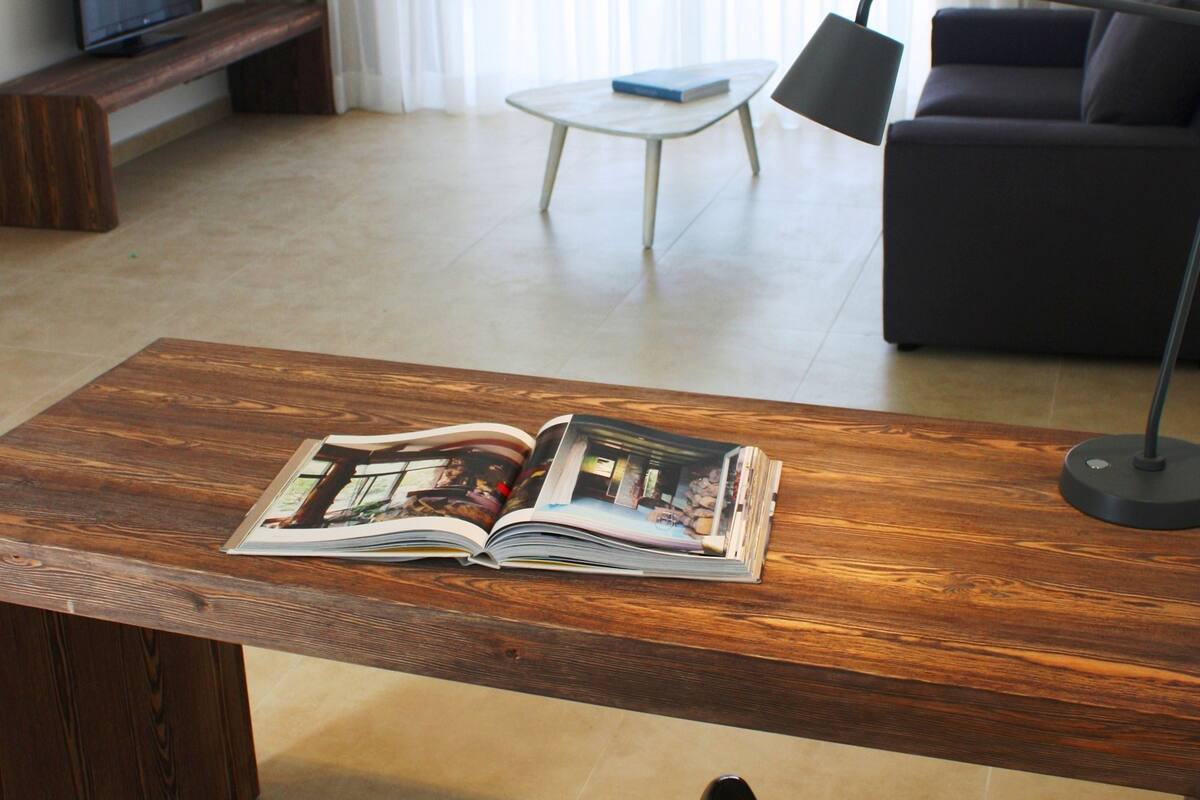 Un salon moderne avec une table basse en bois, un fauteuil noir, un canapé et un téléviseur posé sur un meuble.