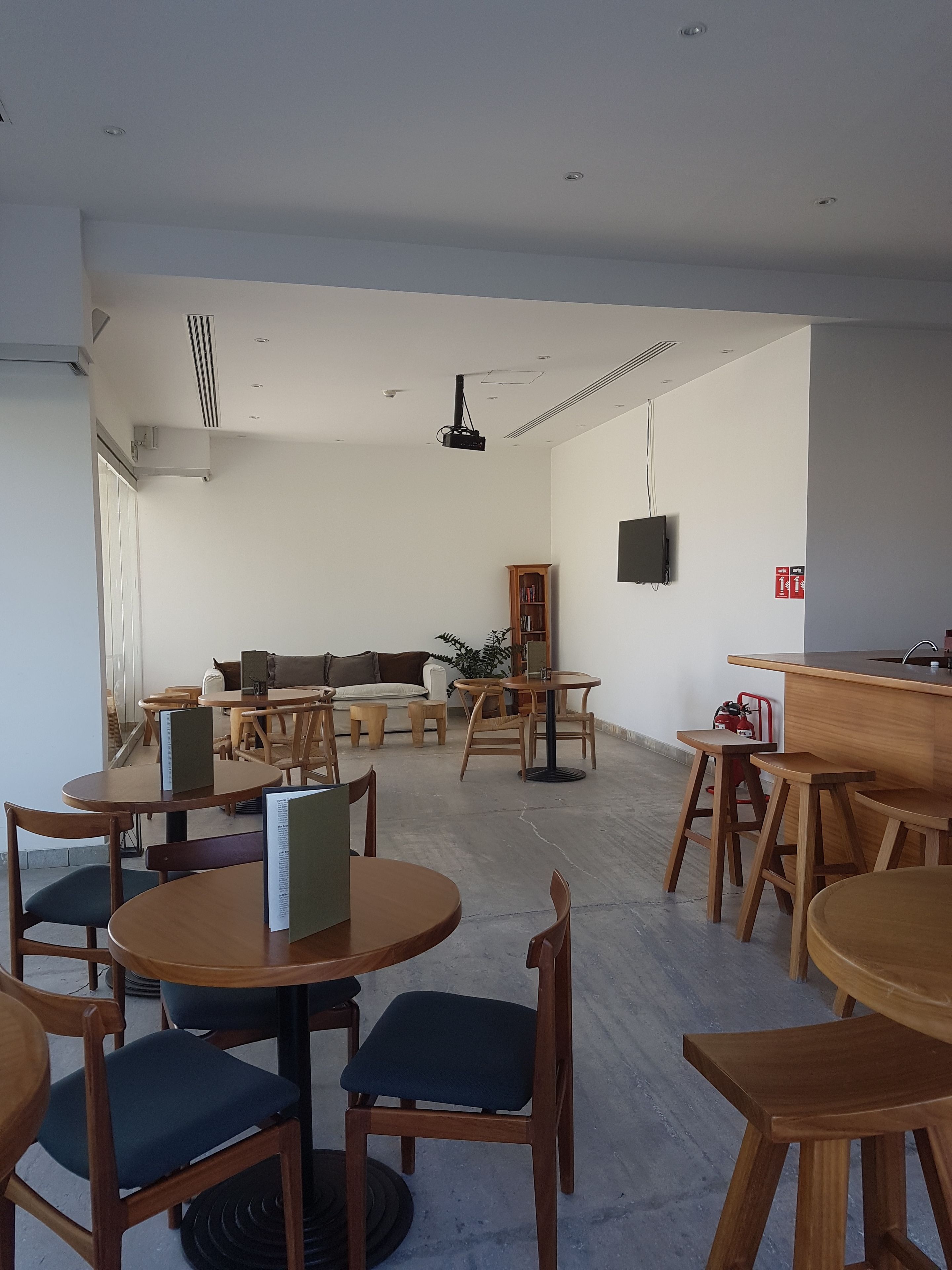 Un intérieur moderne avec des tables et des chaises rondes en bois, un canapé, une bibliothèque et un téléviseur fixé au mur.