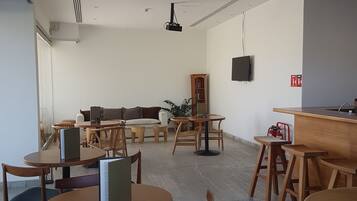 Un intérieur moderne avec des tables et des chaises rondes en bois, un canapé, une bibliothèque et un téléviseur fixé au mur.