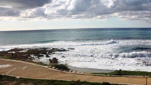 A beach with waves crashing onto the shore, a sandy path, and a rocky outcrop. - Amphora Hotel & Suites (Paphos)