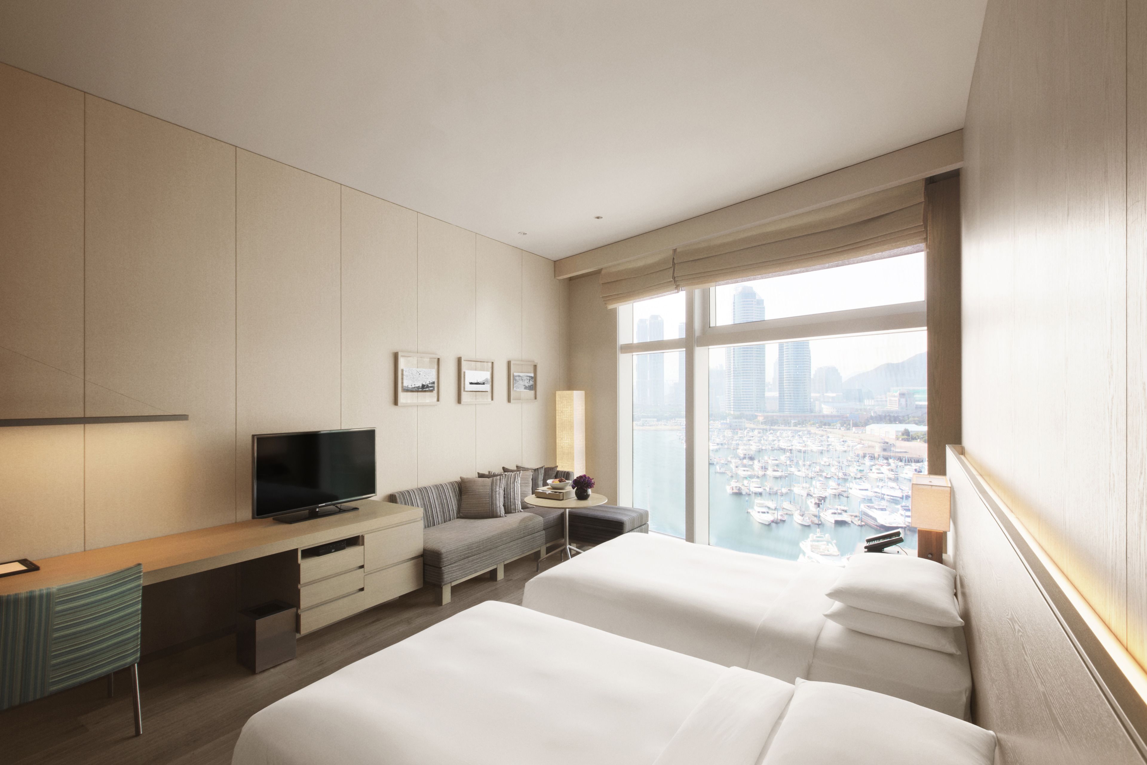 A hotel room with a bed, a TV, a desk, and a view of the city.