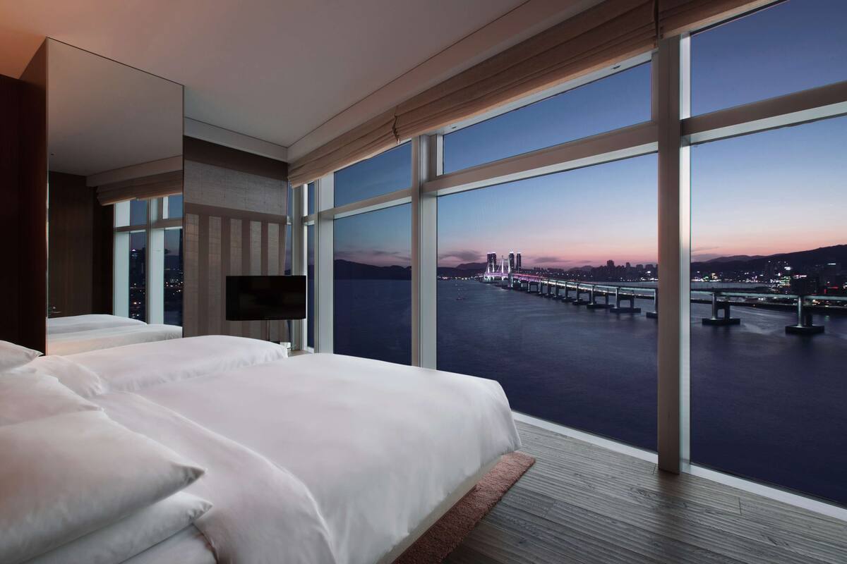 A modern hotel room with a large window offering a view of a bridge and cityscape.