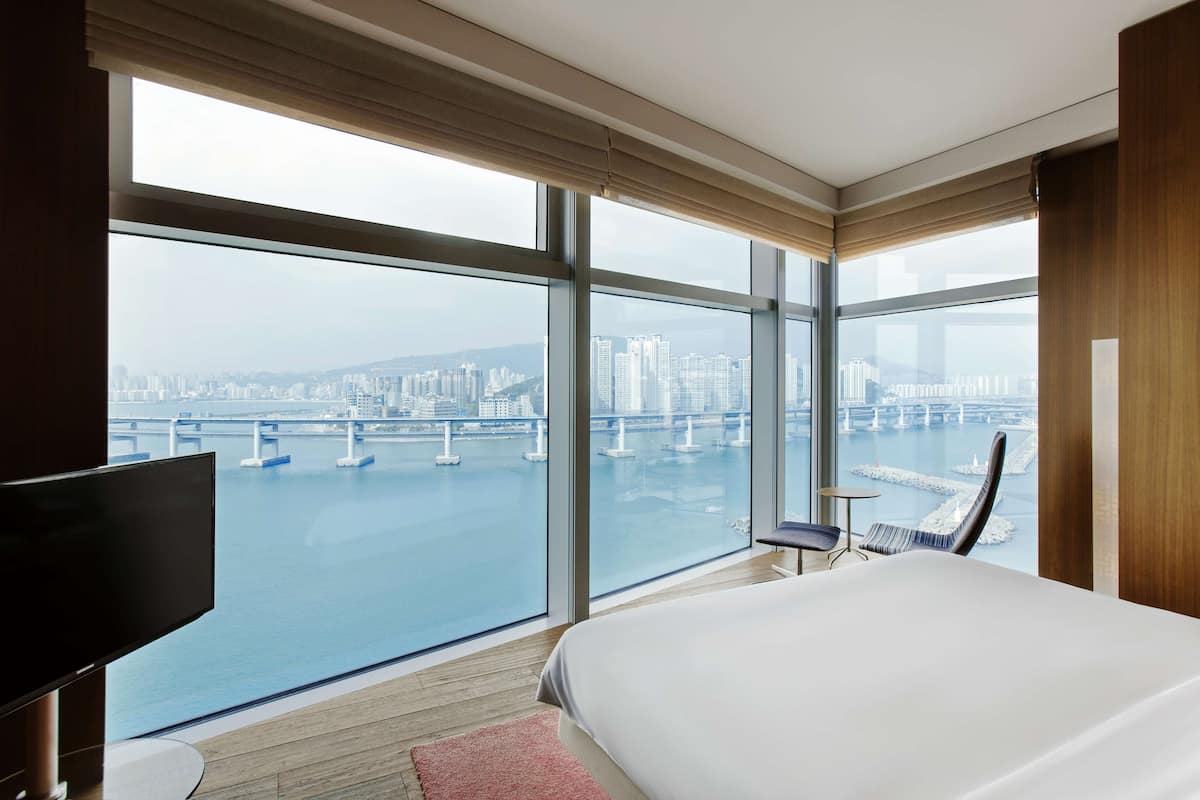 A hotel room with a large window offering a view of a cityscape and a bridge over water.
