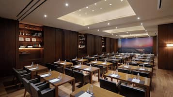 A conference room with multiple tables and chairs, wooden paneling, and a large screen displaying a scenic view.