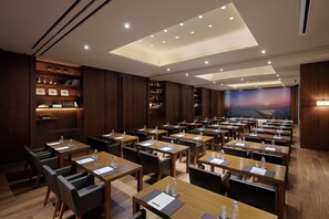 A conference room with multiple tables and chairs, wooden paneling, and a large screen displaying a scenic view.