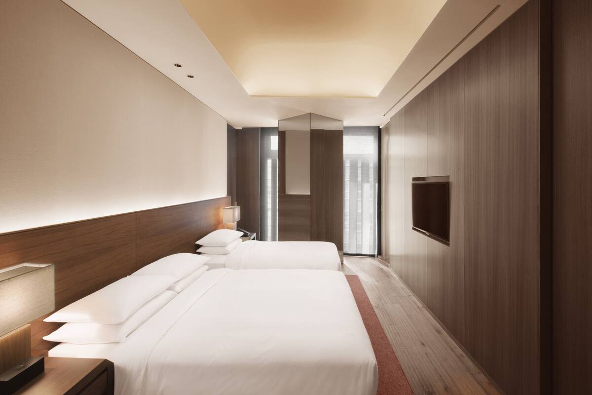 A modern hotel room with a large bed, a TV, and a wooden accent wall.