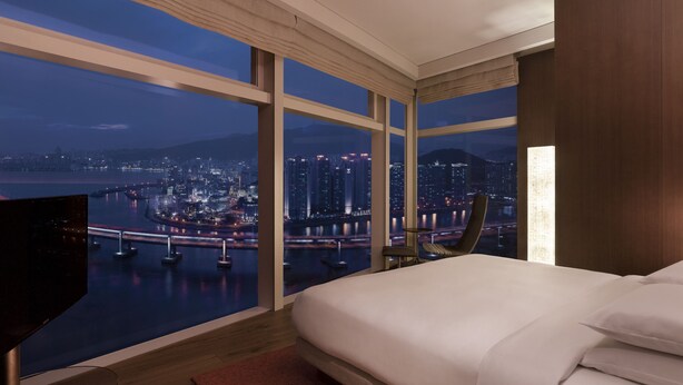 A modern hotel room with a large bed, a TV, and a view of a cityscape at night. - Park Hyatt Busan (Busan)