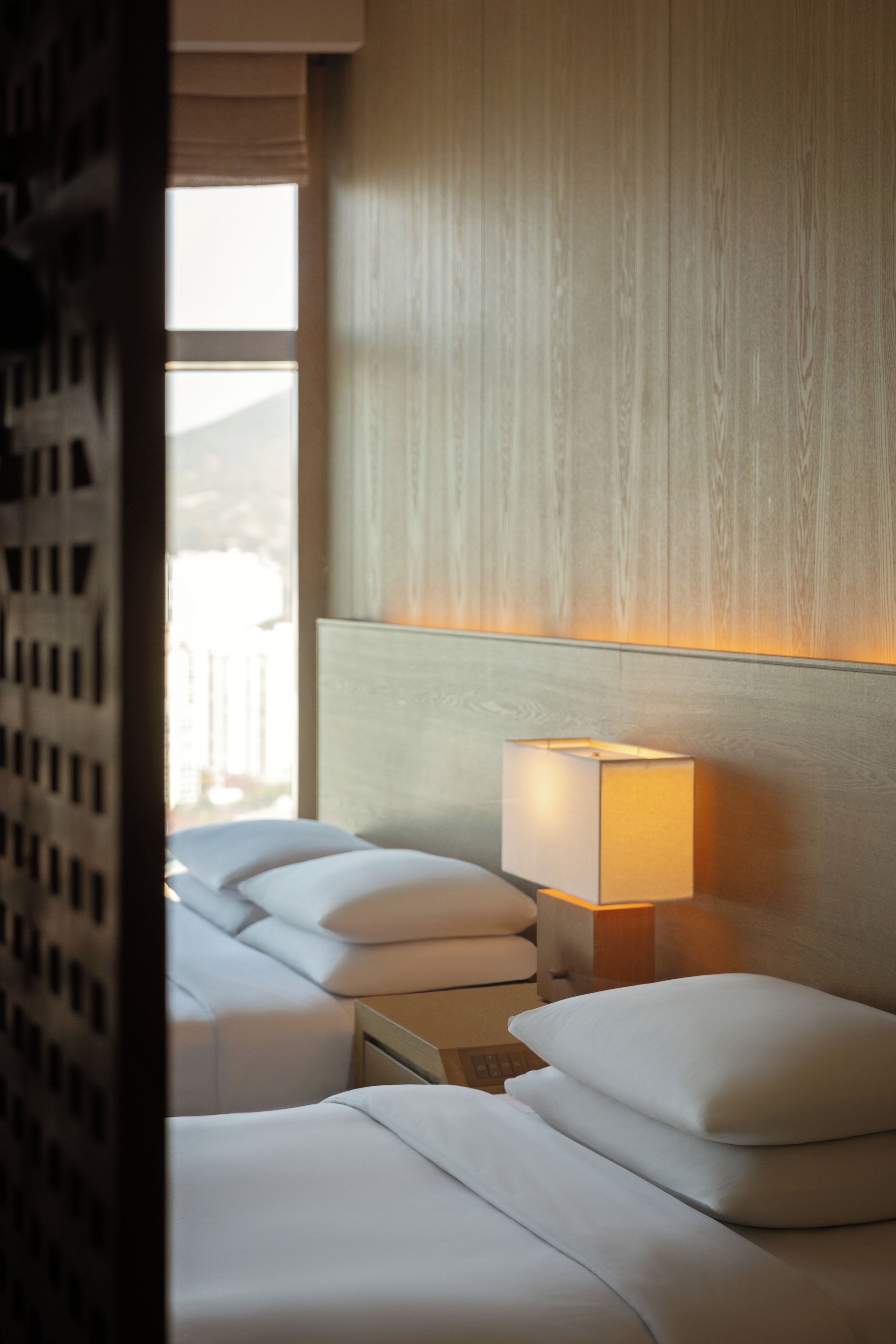 A hotel room with a bed, two bedside tables, a lamp, and a window.