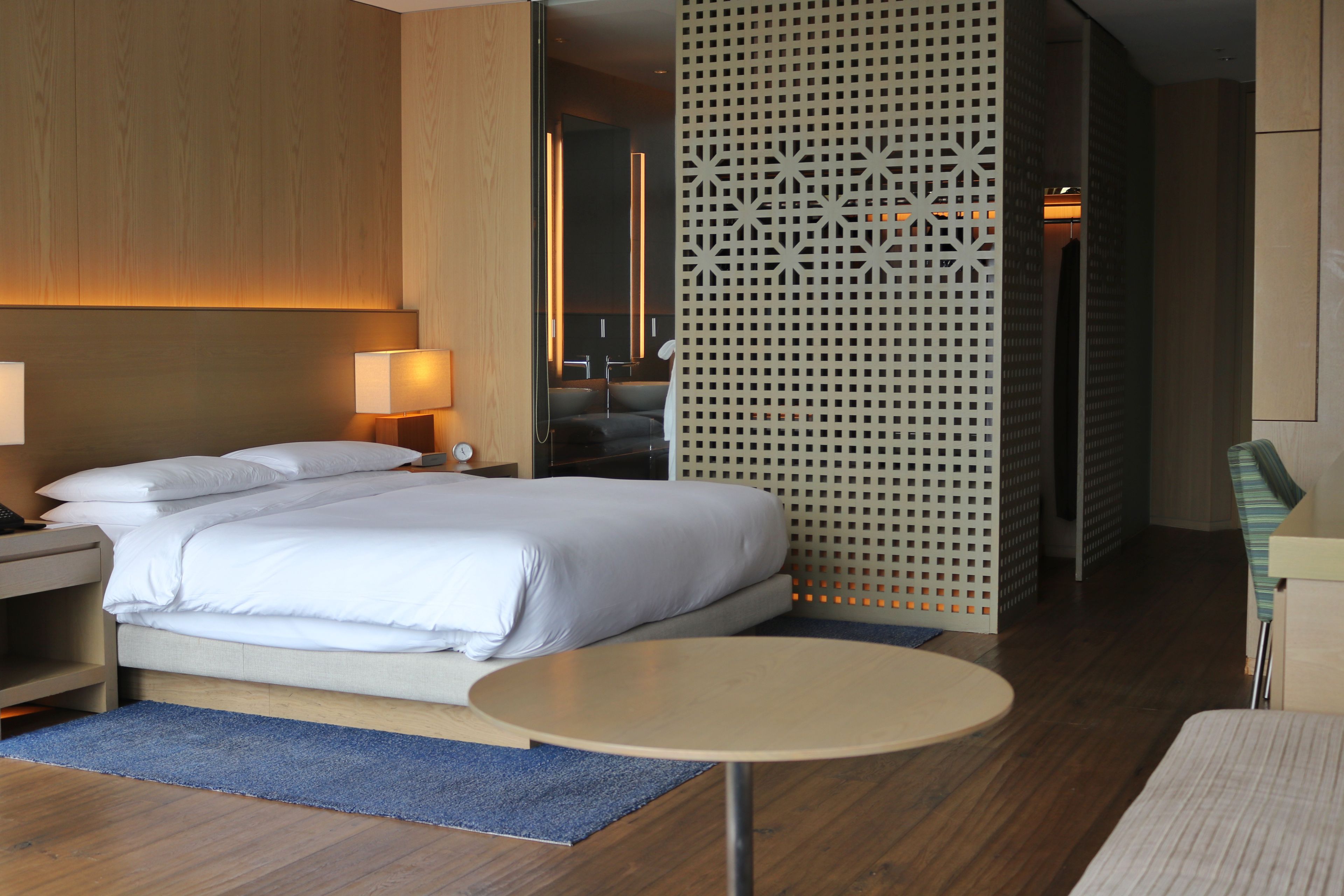 A hotel room with a bed, bedside table, lamp, and a round table.