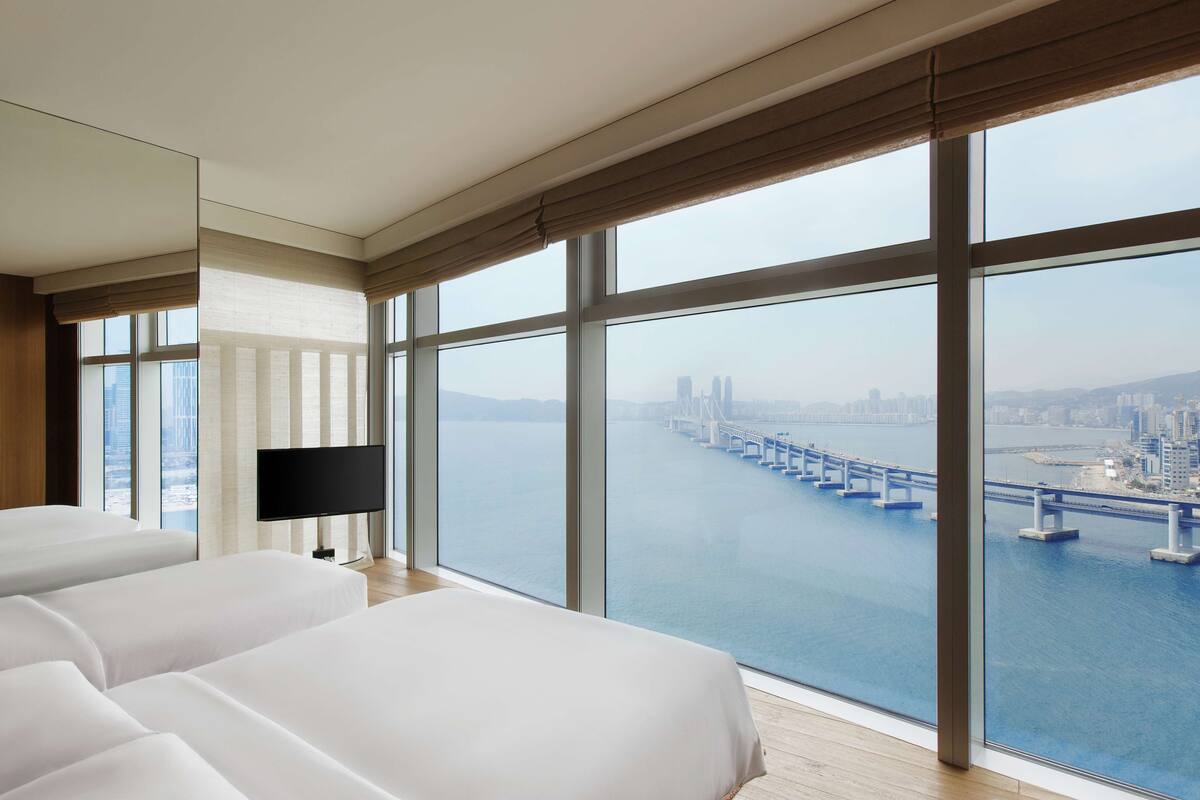 A hotel room with large windows, a flat-screen TV, and a view of a bridge over water.