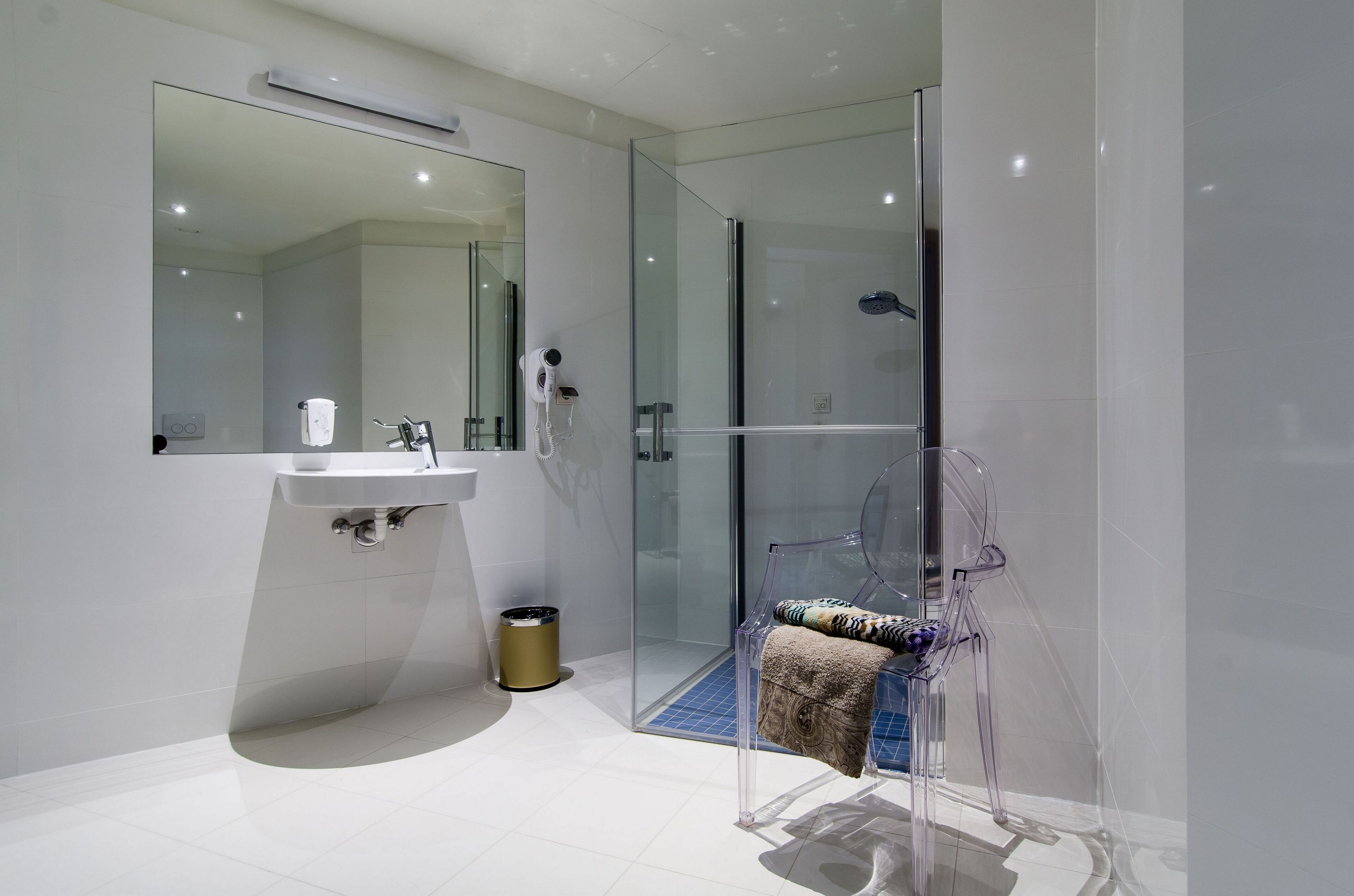 A modern bathroom with a glass shower enclosure, a sink, and a clear chair.