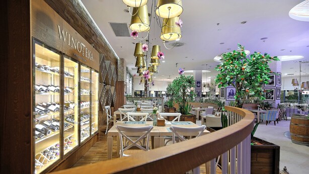 Um saguão de hotel com um display de vinhos, áreas de estar e uma grande planta de interior.