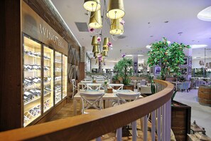 A hotel lobby with a wine selection display, seating areas, and a large indoor plant. - Hotel Rzeszów (Rzeszów)