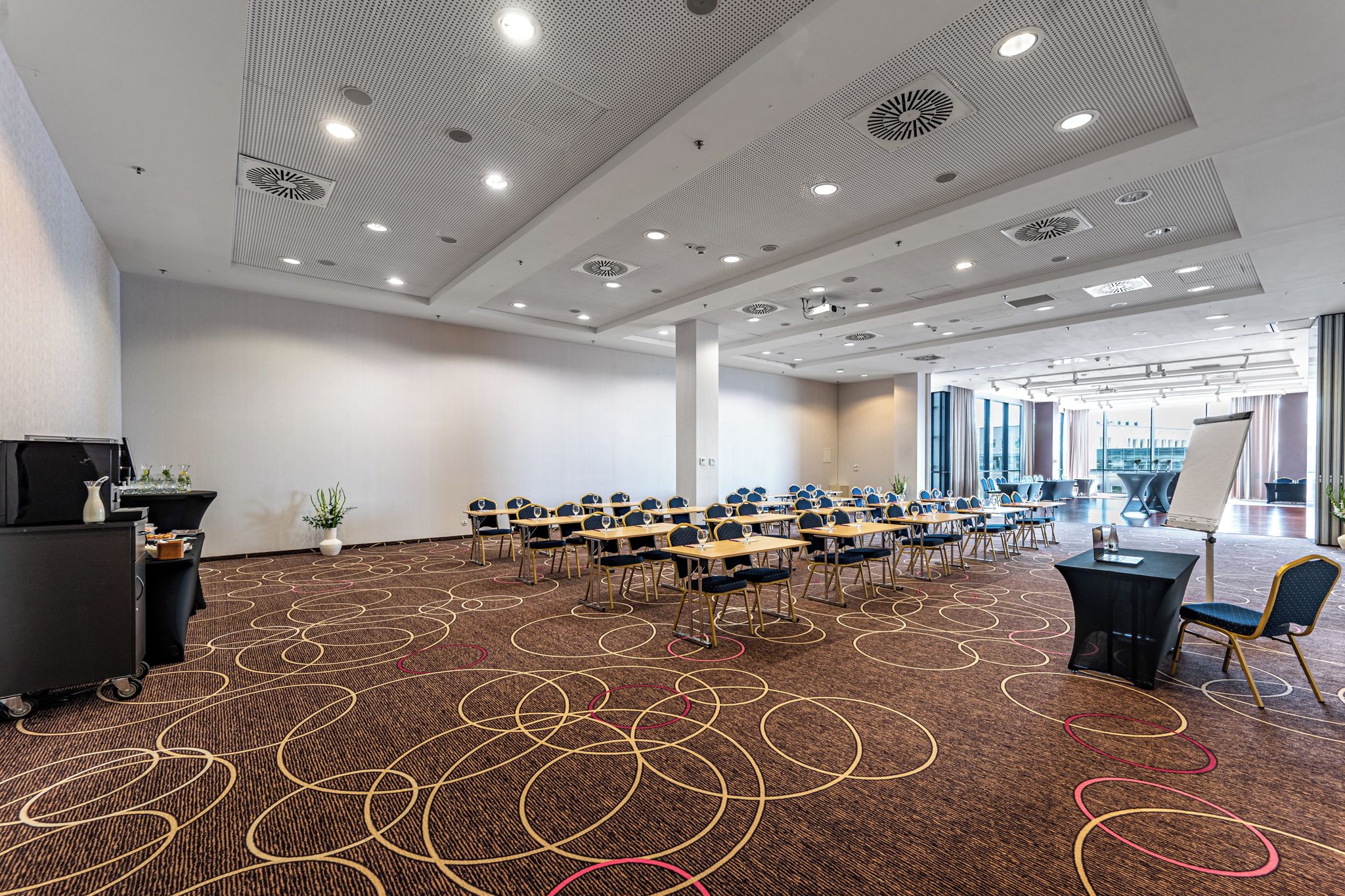 Sala de conferências com uma mesa comprida, cadeiras e um tapete com padrões circulares.