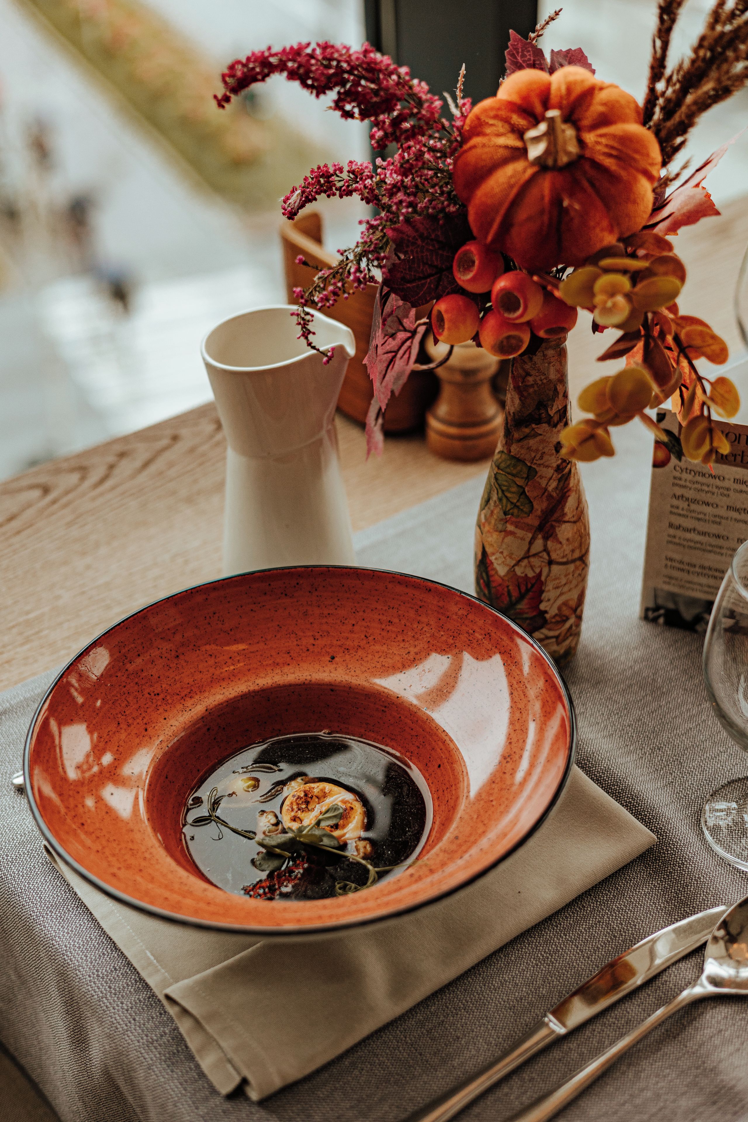 A dining table with a ceramic plate, a vase with flowers, and a menu.