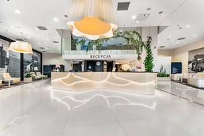 A modern reception desk with a 'RECEPTICA' sign, surrounded by seating and a large window.