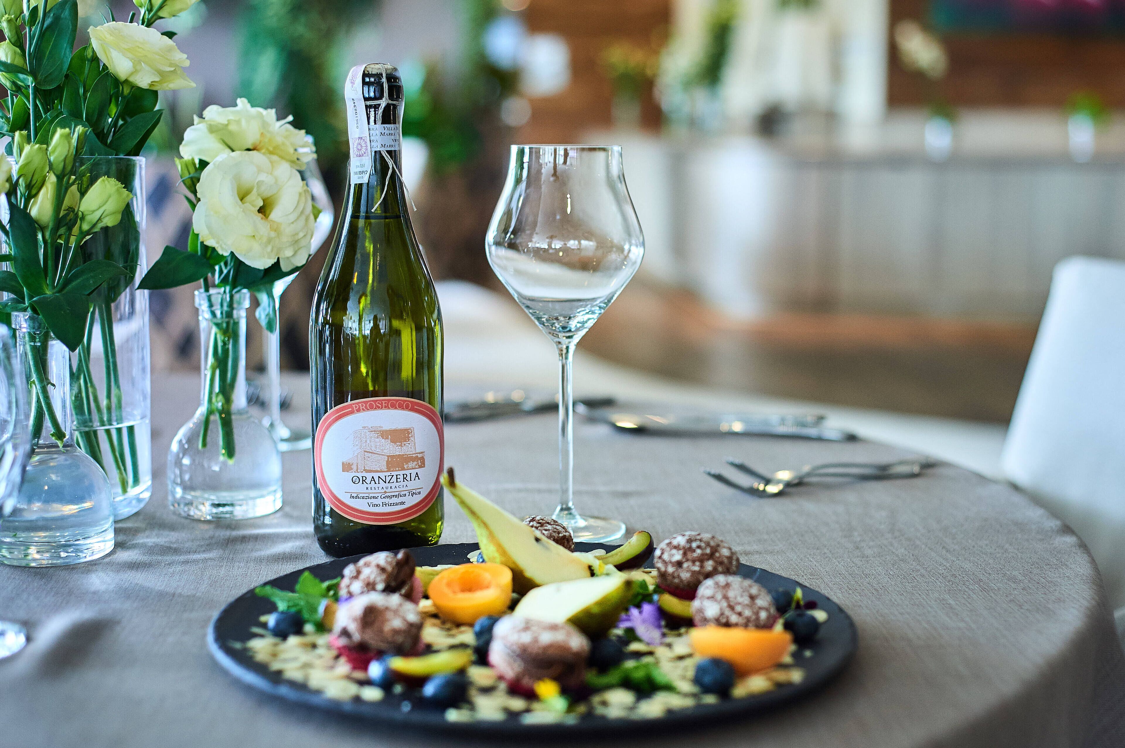 A table with a bottle of Prosecco, a wine glass, and a plate of food.