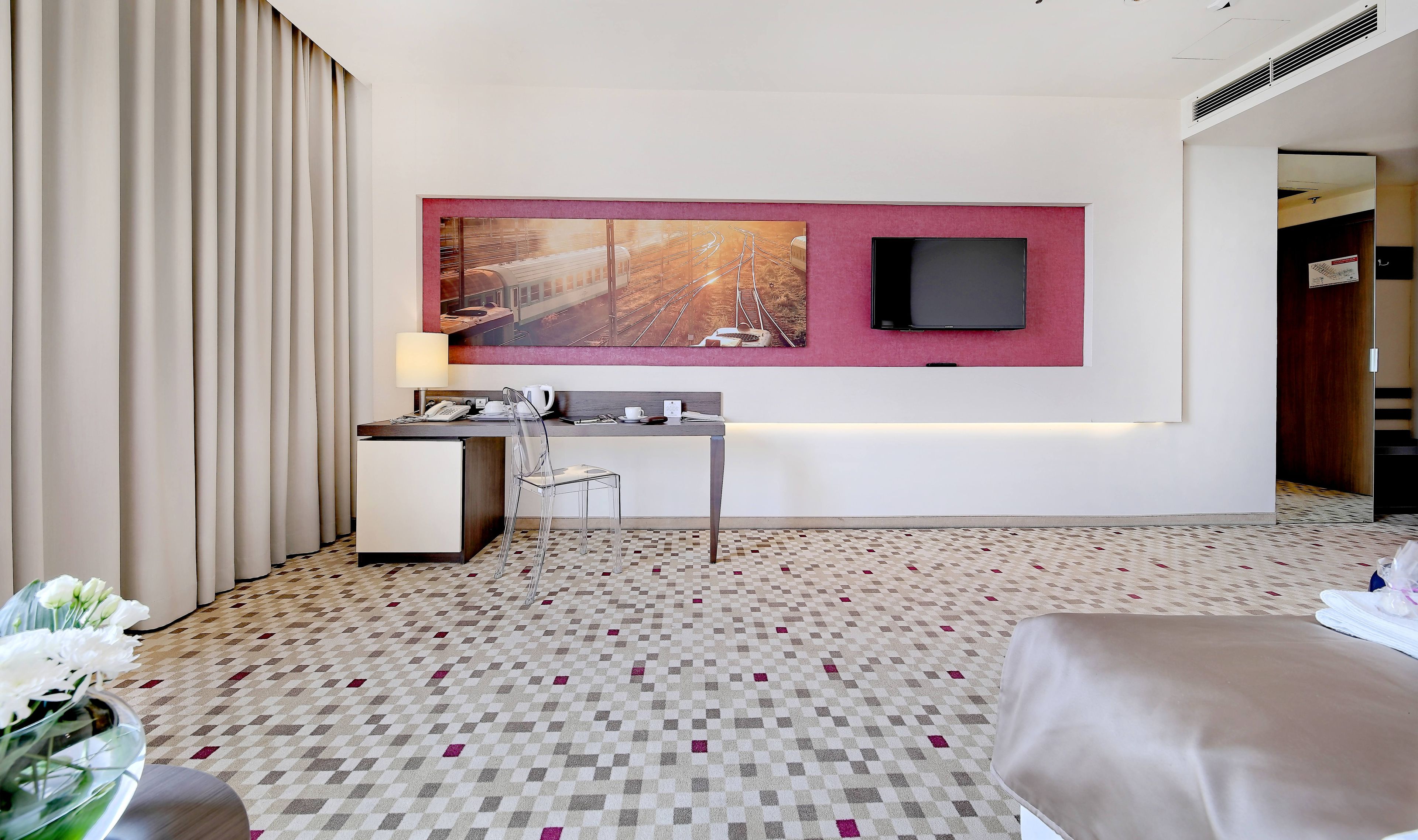 Une chambre d’hôtel avec un lit, un bureau, une chaise, un téléviseur à écran plat, un tableau et un sol à motifs.