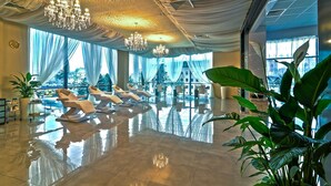 Um hall luxuoso com piso refletivo, cortinas elegantes e várias áreas de estar com cadeiras.