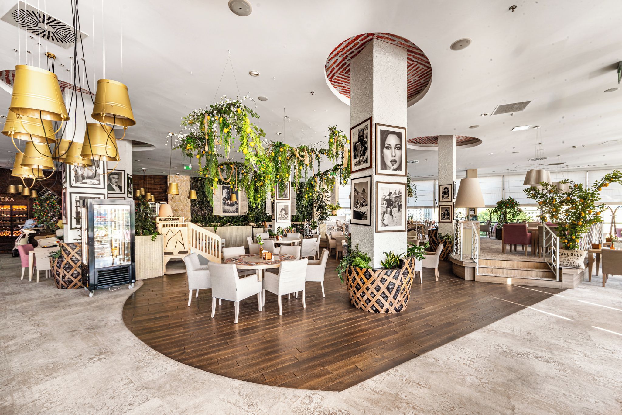 Un hall de hotel espacioso con una zona de estar central, múltiples lámparas colgantes y diversas plantas.
