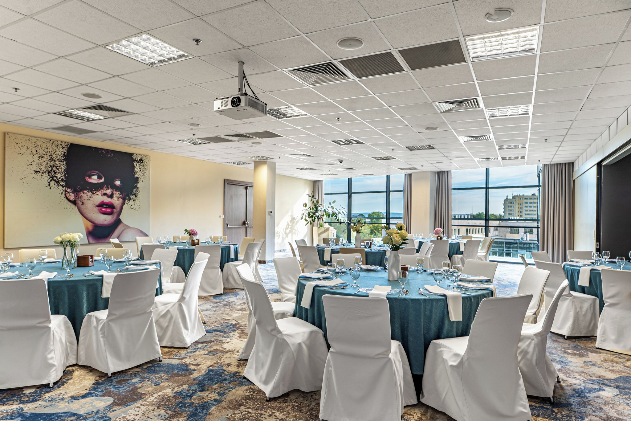 Un salón de conferencias con mesas redondas, sillas blancas y un gran mural en la pared.