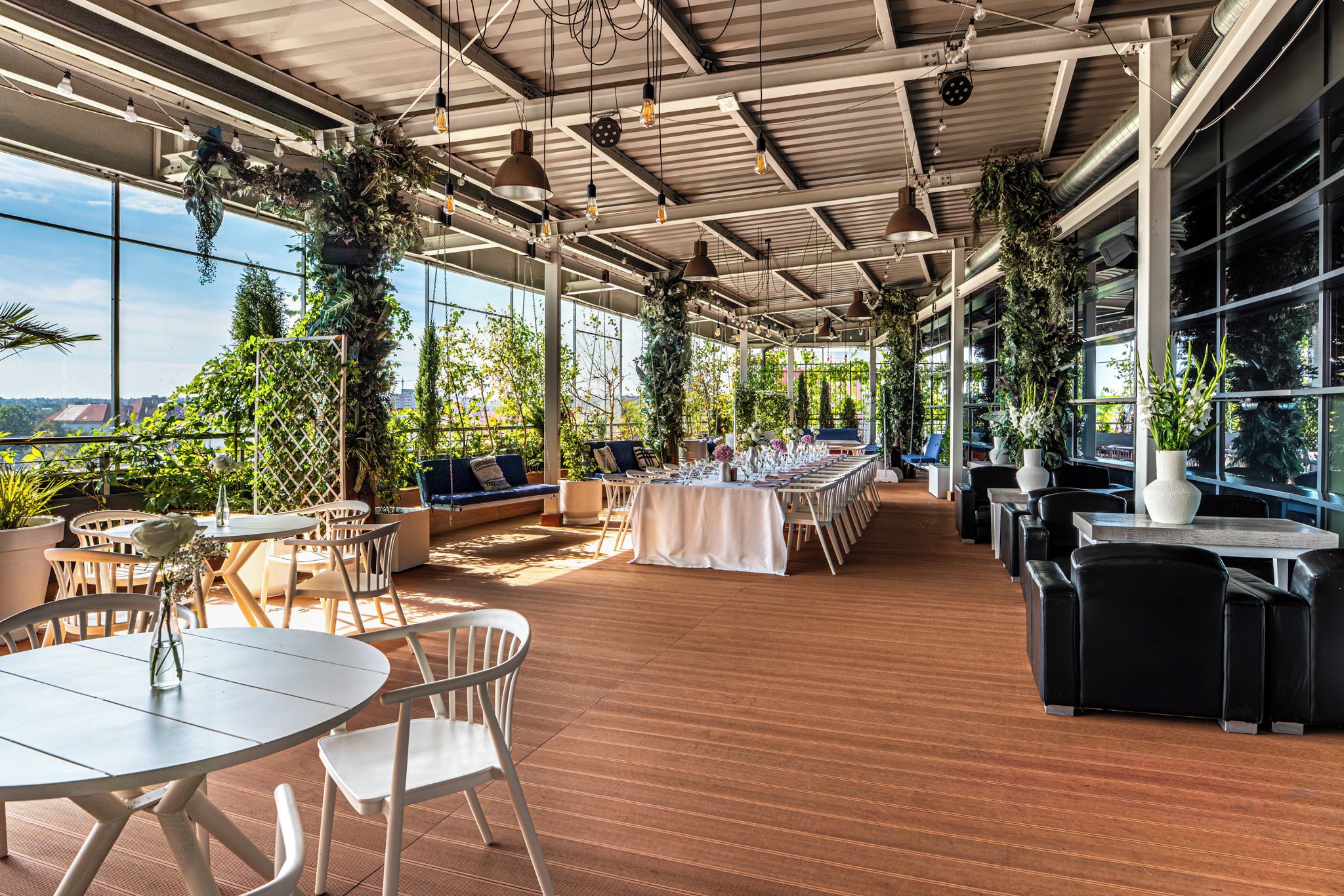 An indoor dining area with tables and chairs, large windows, and hanging plants.