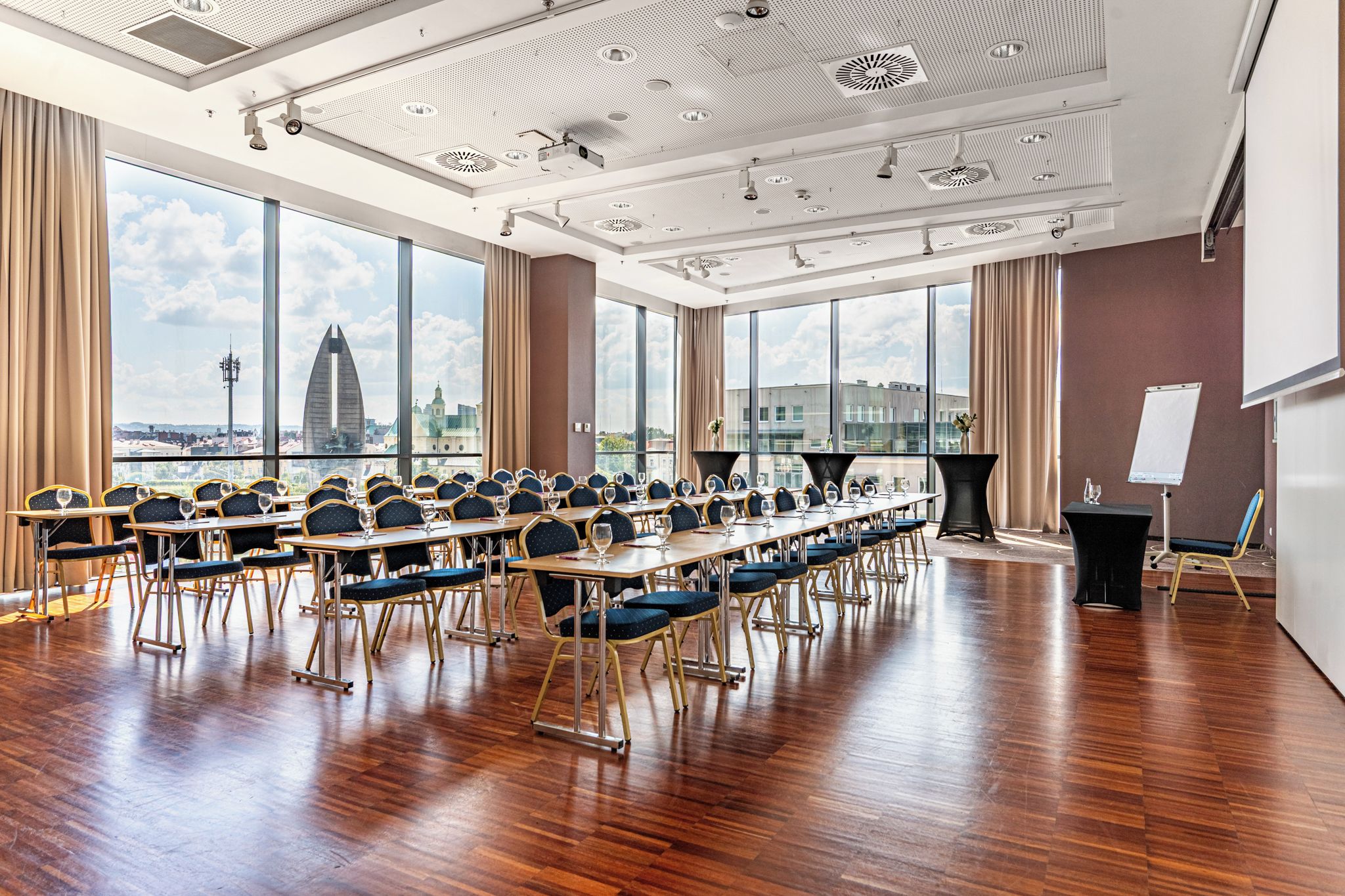 Un salón de conferencias con una larga mesa, sillas, un atril y un ventanal con vista a la ciudad.
