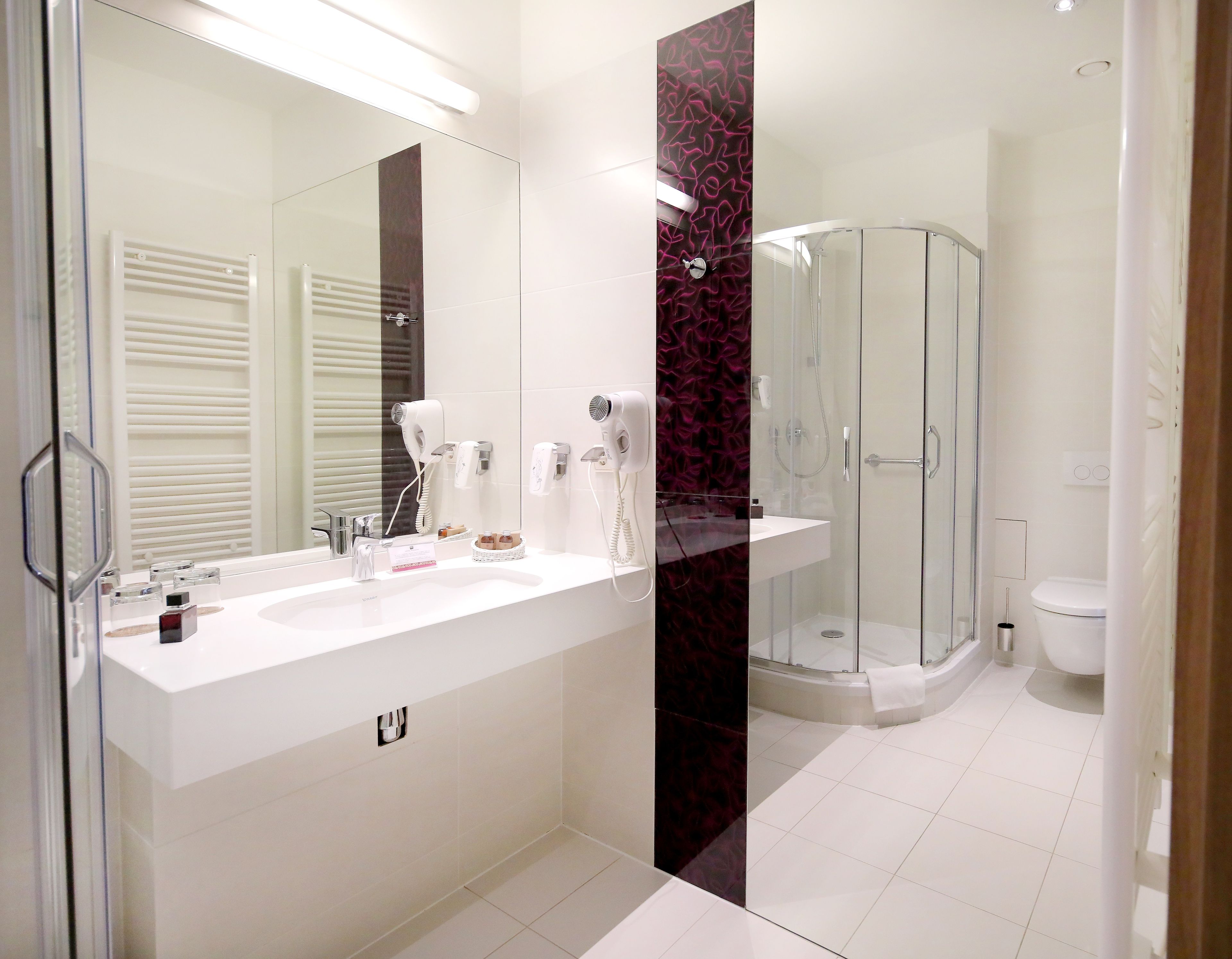 A modern bathroom with a glass shower enclosure, a white sink with a mirror, and a vanity with toiletries.