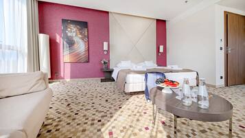 Una camera d'albergo con un letto, un tavolino con frutta e bottiglie d'acqua, un divano e un quadro appeso al muro.