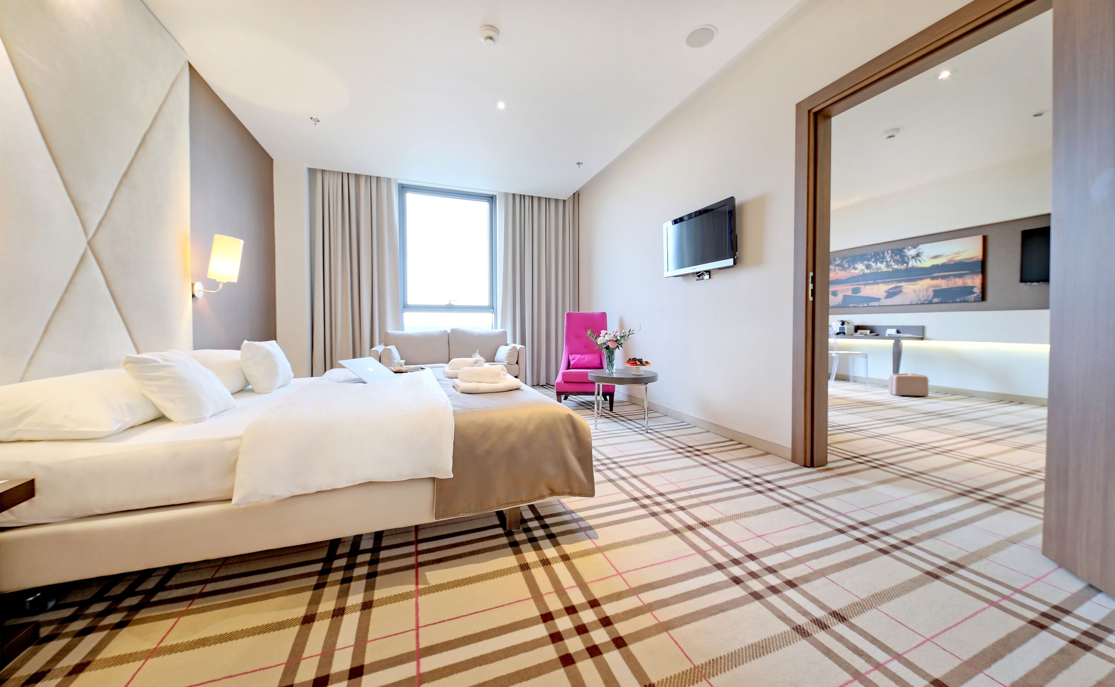 A hotel room with a bed, a desk, a chair, a TV, and a large window.