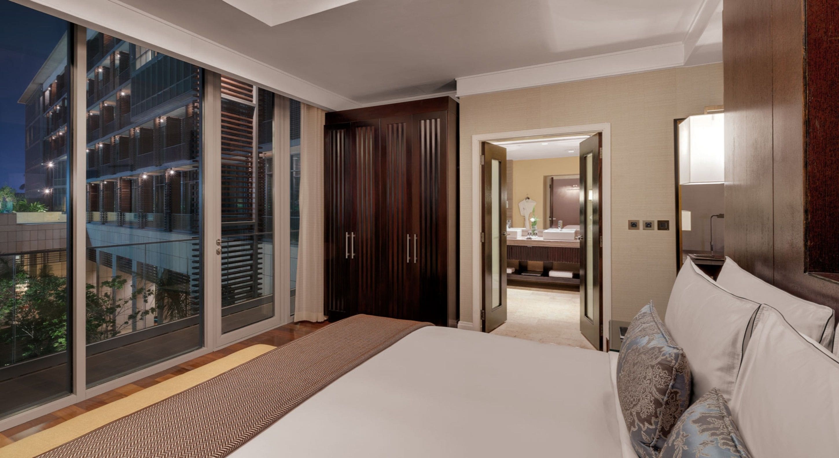 Ein modernes Hotelzimmer mit einem großen Bett, einem begehbaren Kleiderschrank und einer Schiebetür zu einem Außenbalkon.