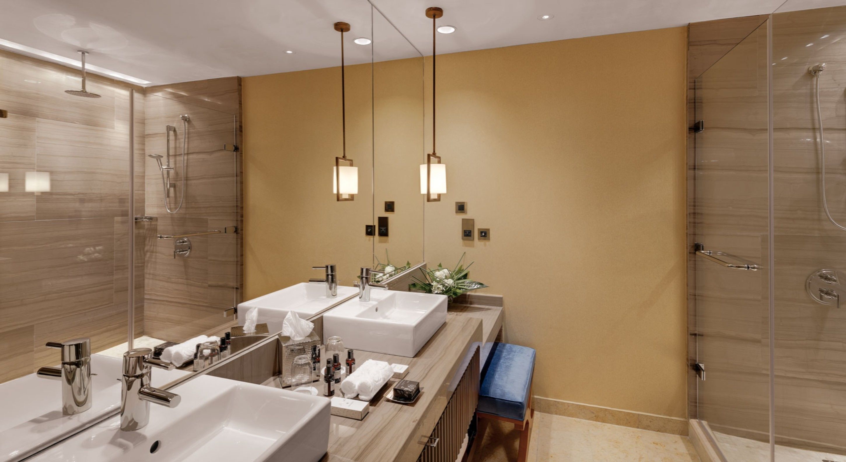 A modern bathroom with two sinks, a glass shower enclosure, and pendant lighting.